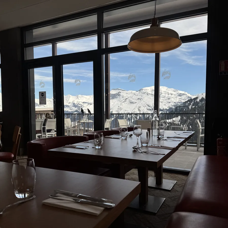 Restaurante do resort com mesas postas diante de um janelão com vista para o maciço nevado