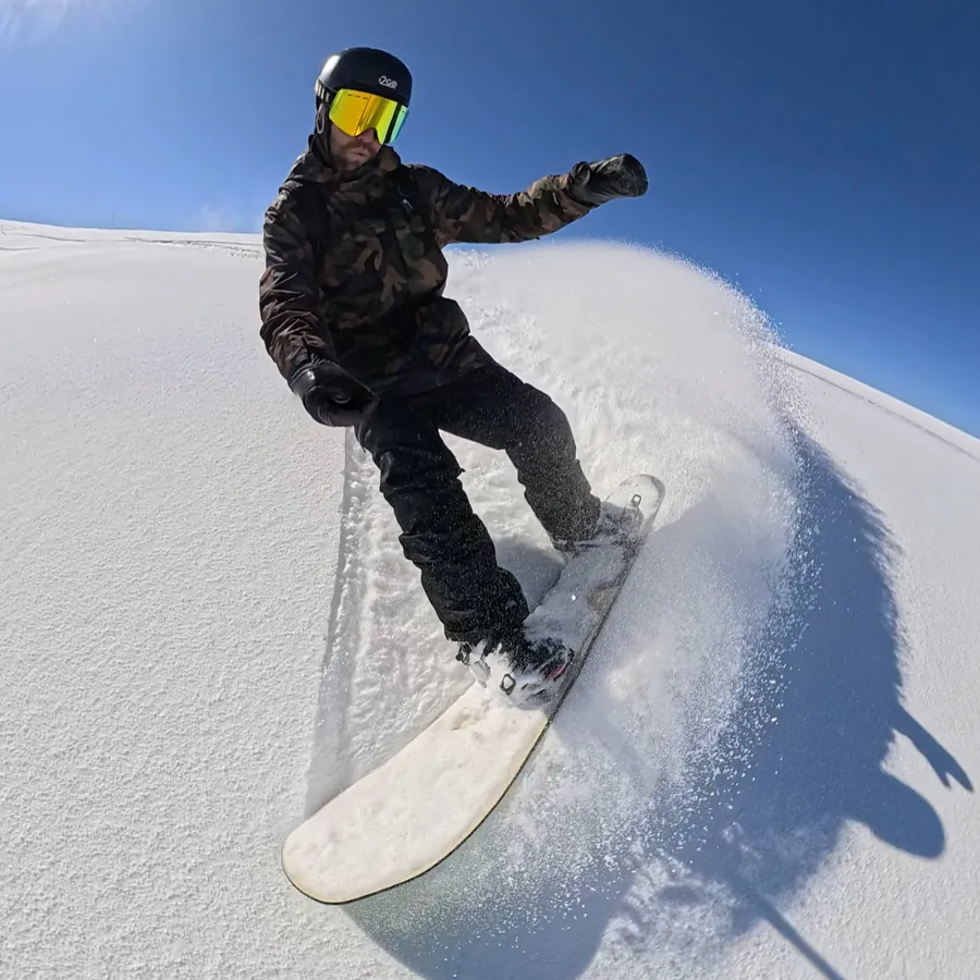 Snowboarder descendo em neve fresca sob o sol, com a sombra projetada na encosta