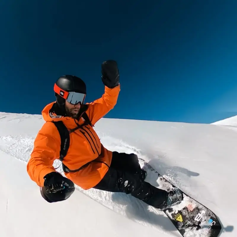 Snowboarder da ProSnowLife numa curva na neve, com céu azul ao fundo